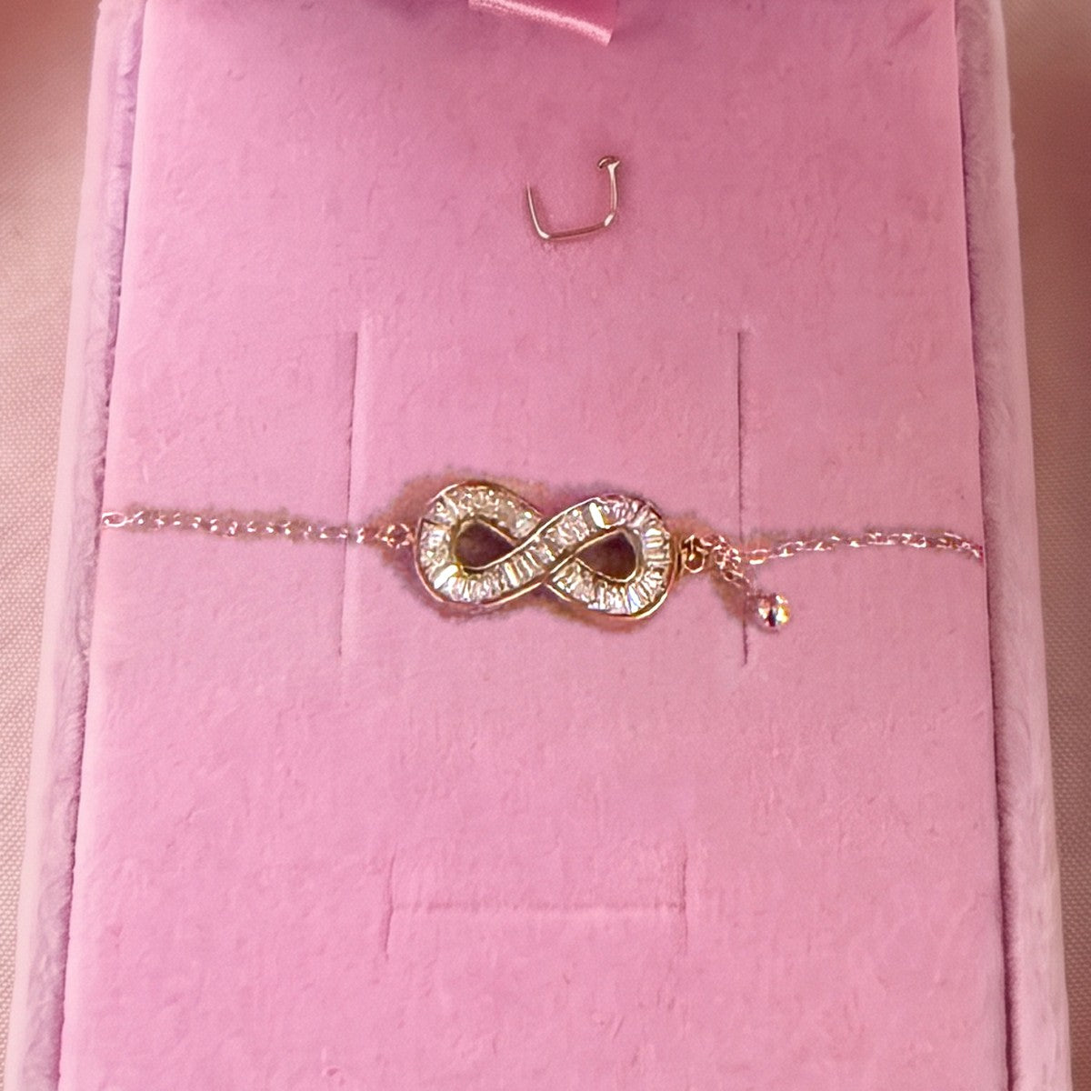 Gros plan : bracelet doré à symbole infini serti, posé sur velours rose