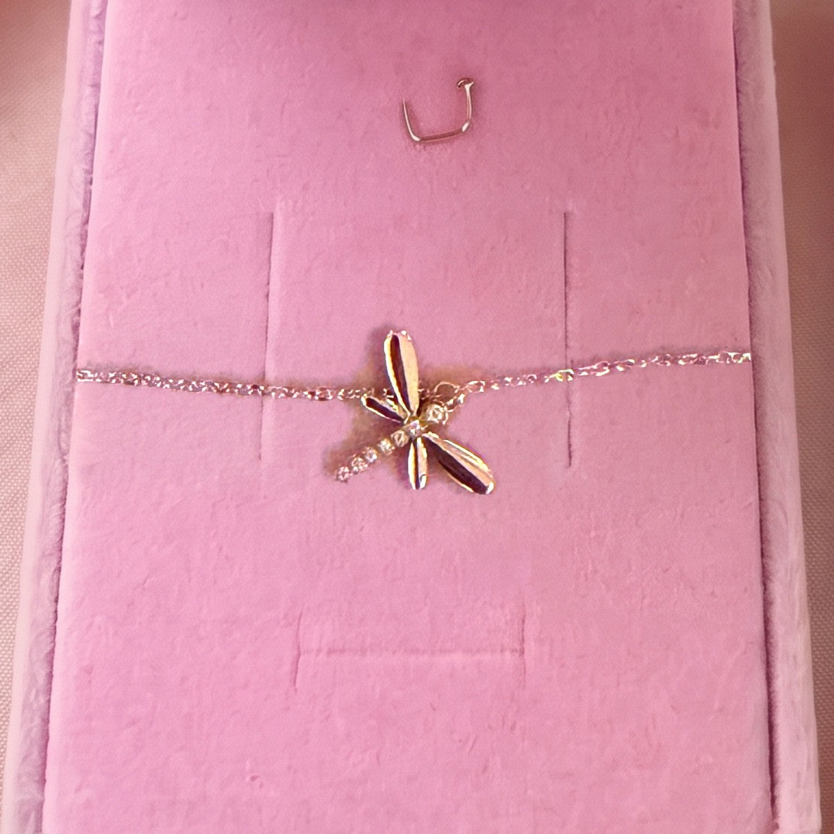 Gros plan : bracelet doré à libellule sertie, posé sur velours rose