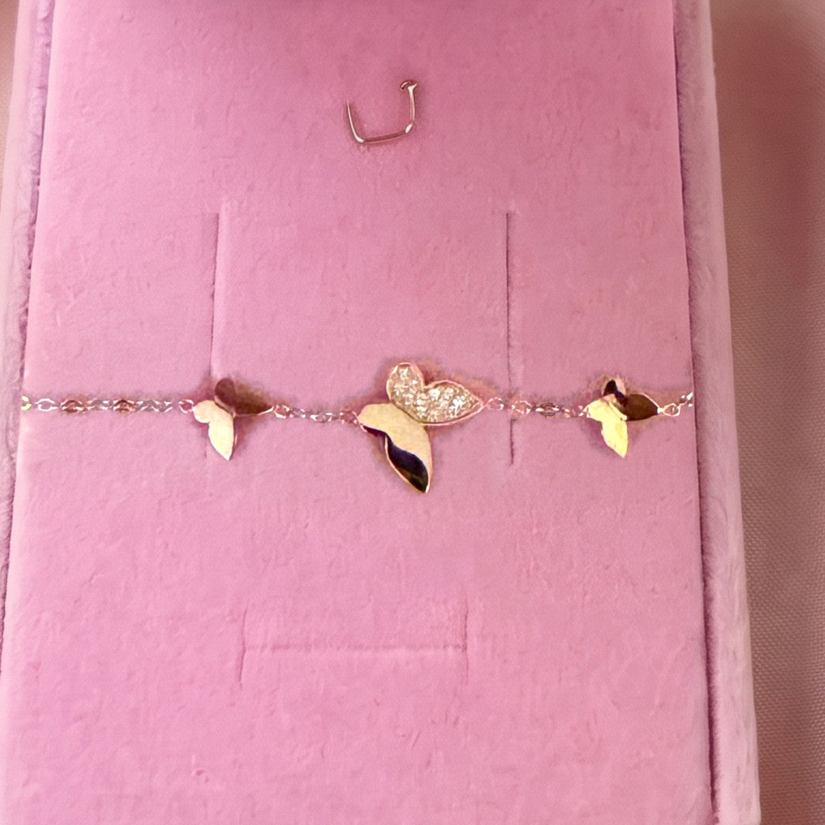 Gros plan : bracelet doré à trois papillons, posé sur velours rose