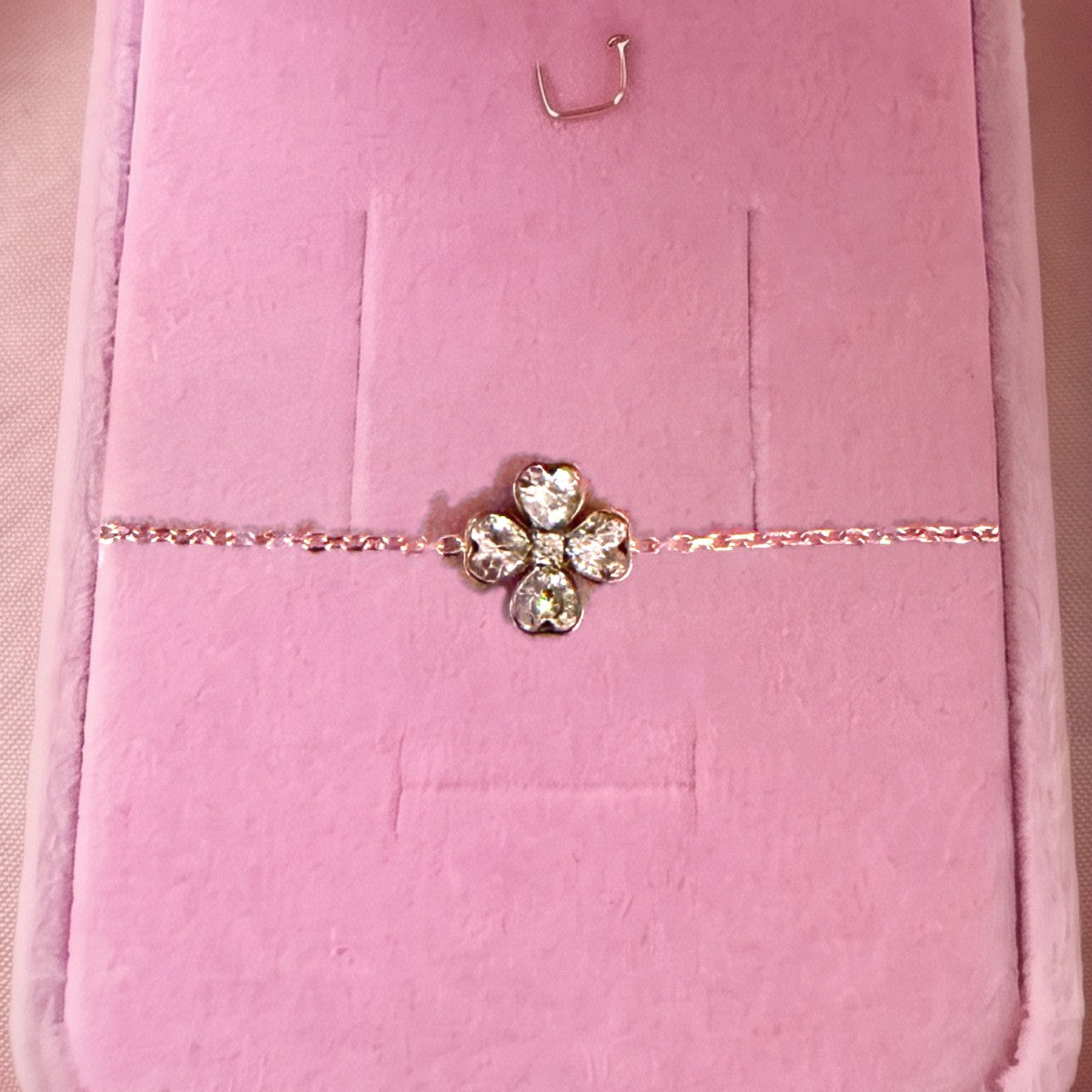 Gros plan : bracelet doré à trèfle de quatre pierres en cœur, posé sur velours rose