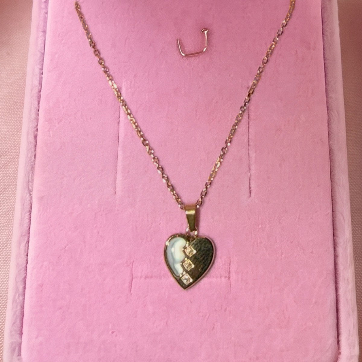 Gros plan : collier à pendentif cœur, moitié blanche et trois petites pierres, posé sur velours rose