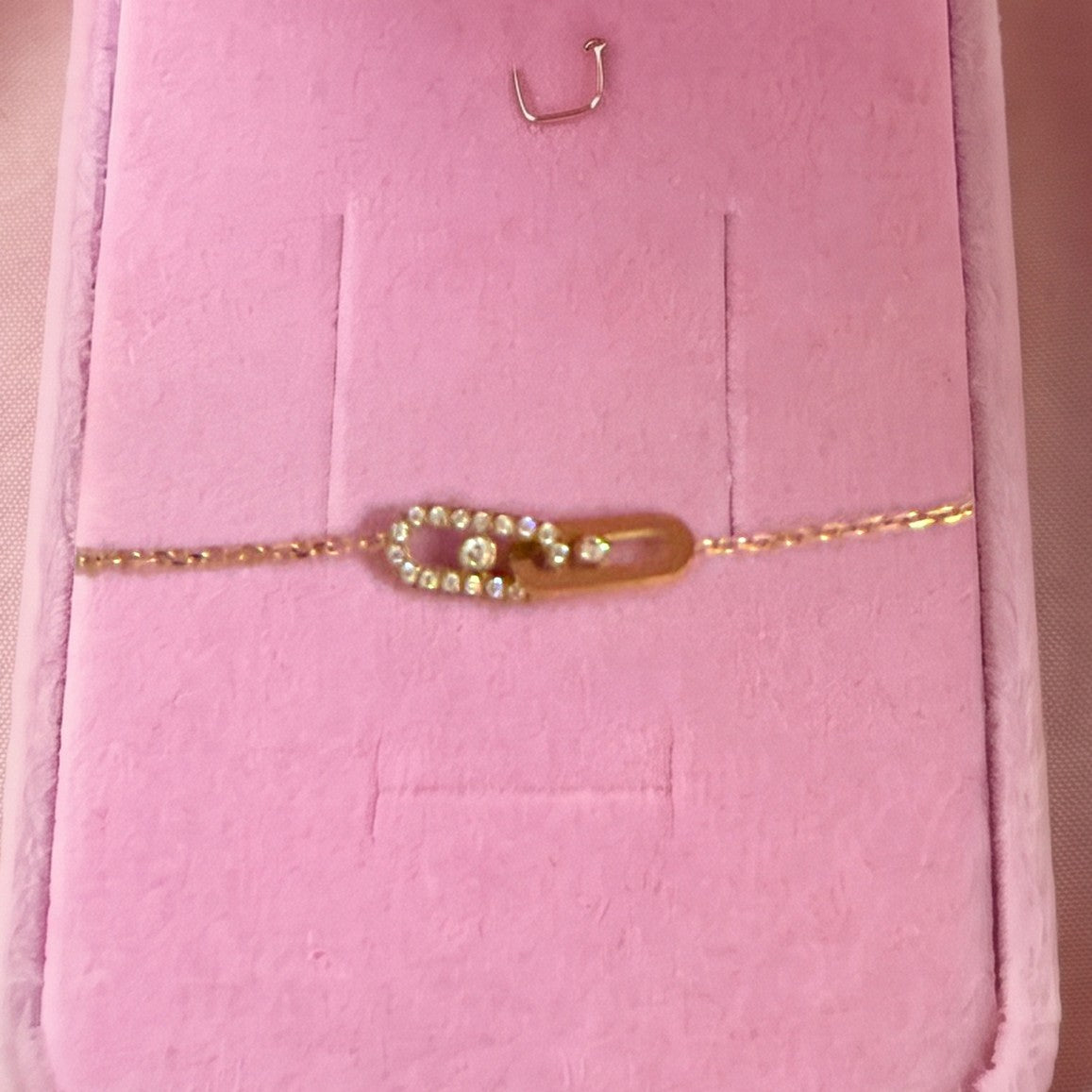Gros plan : bracelet doré à deux anneaux ovales entrelacés, posé sur velours rose