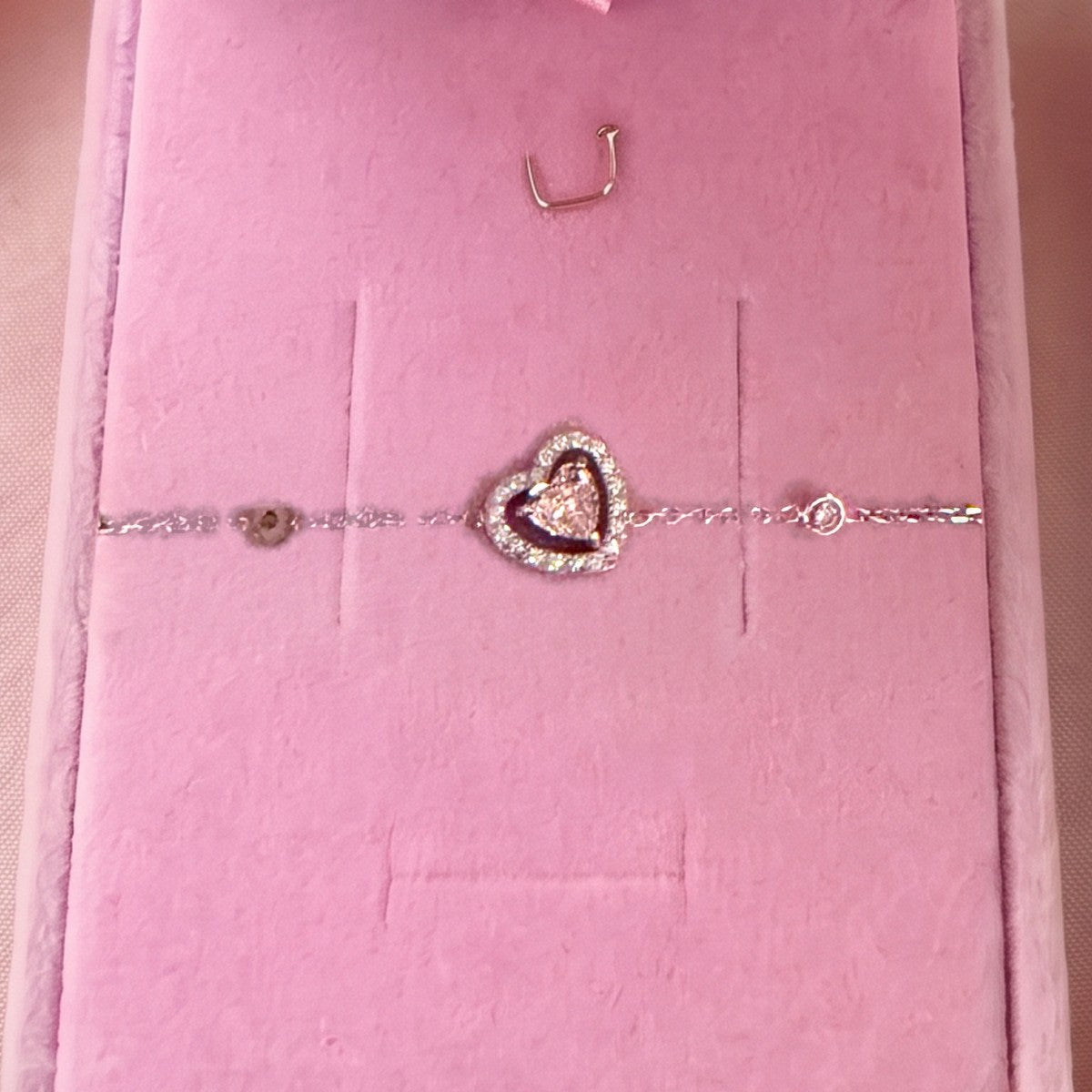 Gros plan : bracelet argenté à cœur entouré d'un contour pavé, posé sur velours rose