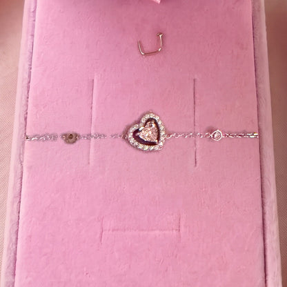 Gros plan : bracelet argenté à cœur entouré d'un contour pavé, posé sur velours rose