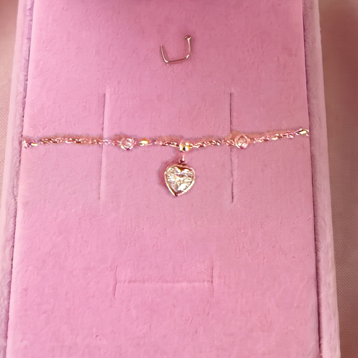 Gros plan du bracelet doré à pendentif cœur, pierre blanche, sur velours rose