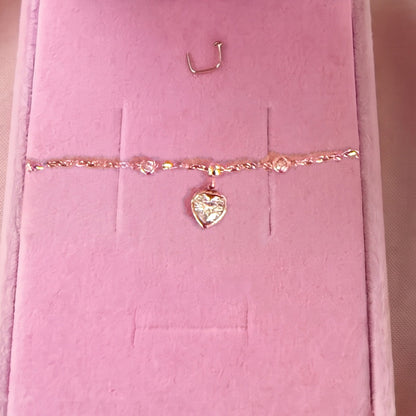 Gros plan du bracelet doré à pendentif cœur, pierre blanche, sur velours rose