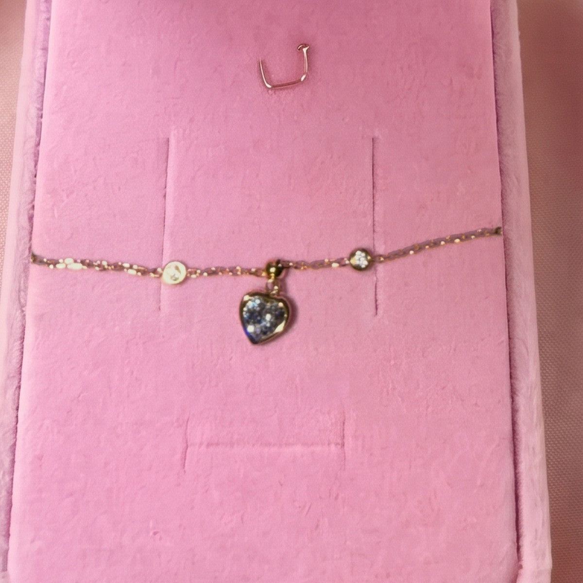 Gros plan du bracelet doré à pendentif cœur, pierre violette, sur velours rose