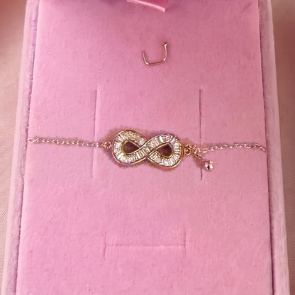 Gros plan : bracelet doré à symbole infini serti, posé sur velours rose