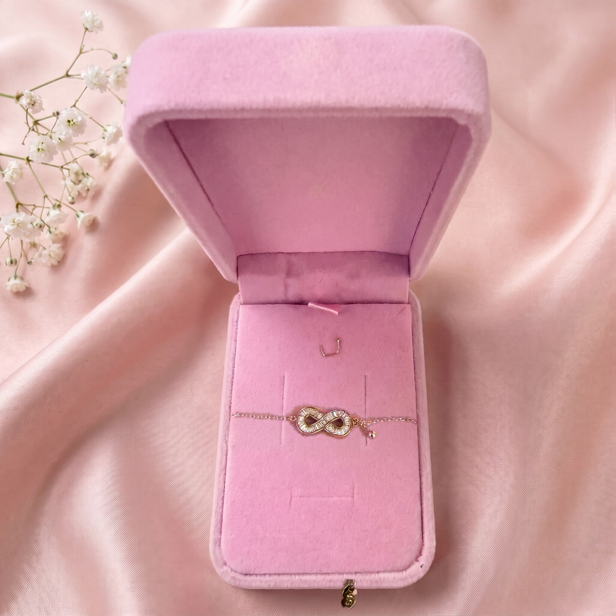 Bracelet infini dans un écrin en velours rose ouvert, posé sur un satin rose