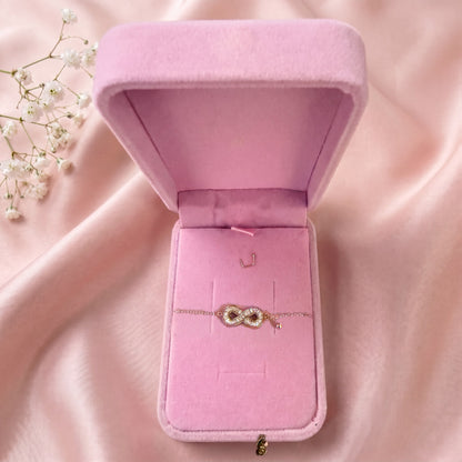 Bracelet infini dans un écrin en velours rose ouvert, posé sur un satin rose