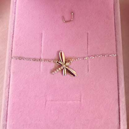Gros plan : bracelet doré à libellule sertie, posé sur velours rose
