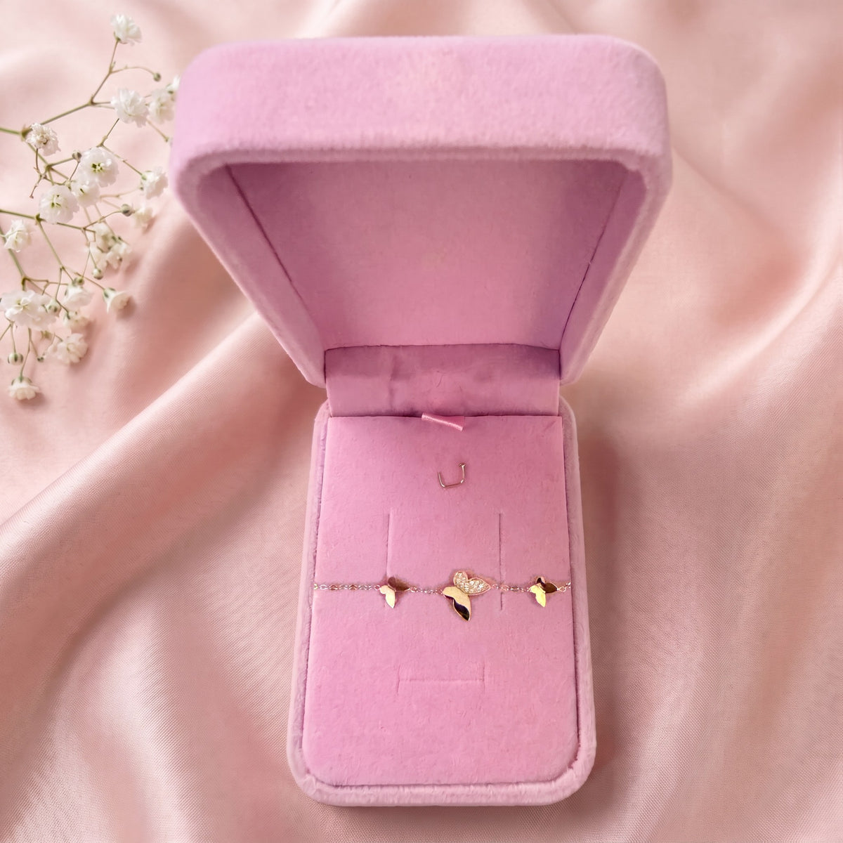 Bracelet papillons dans un écrin en velours rose ouvert, posé sur un satin rose