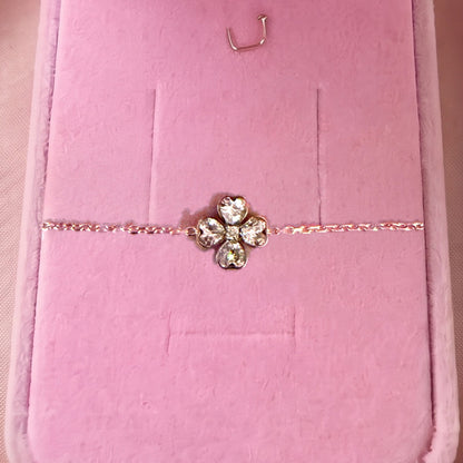 Gros plan : bracelet doré à trèfle de quatre pierres en cœur, posé sur velours rose