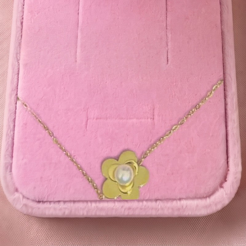 Gros plan : collier à pendentif fleur dorée et perle blanche, posé sur velours rose