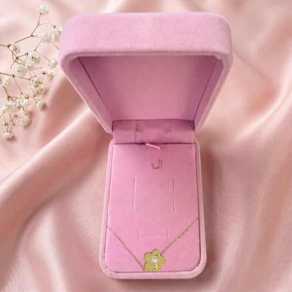 Collier fleur et perle dans un écrin en velours rose ouvert, posé sur un satin rose