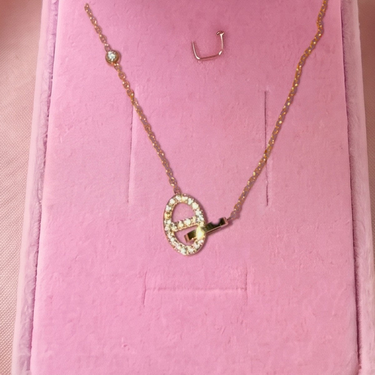 Gros plan : collier doré à pendentif maillon ovale pavé, posé sur velours rose