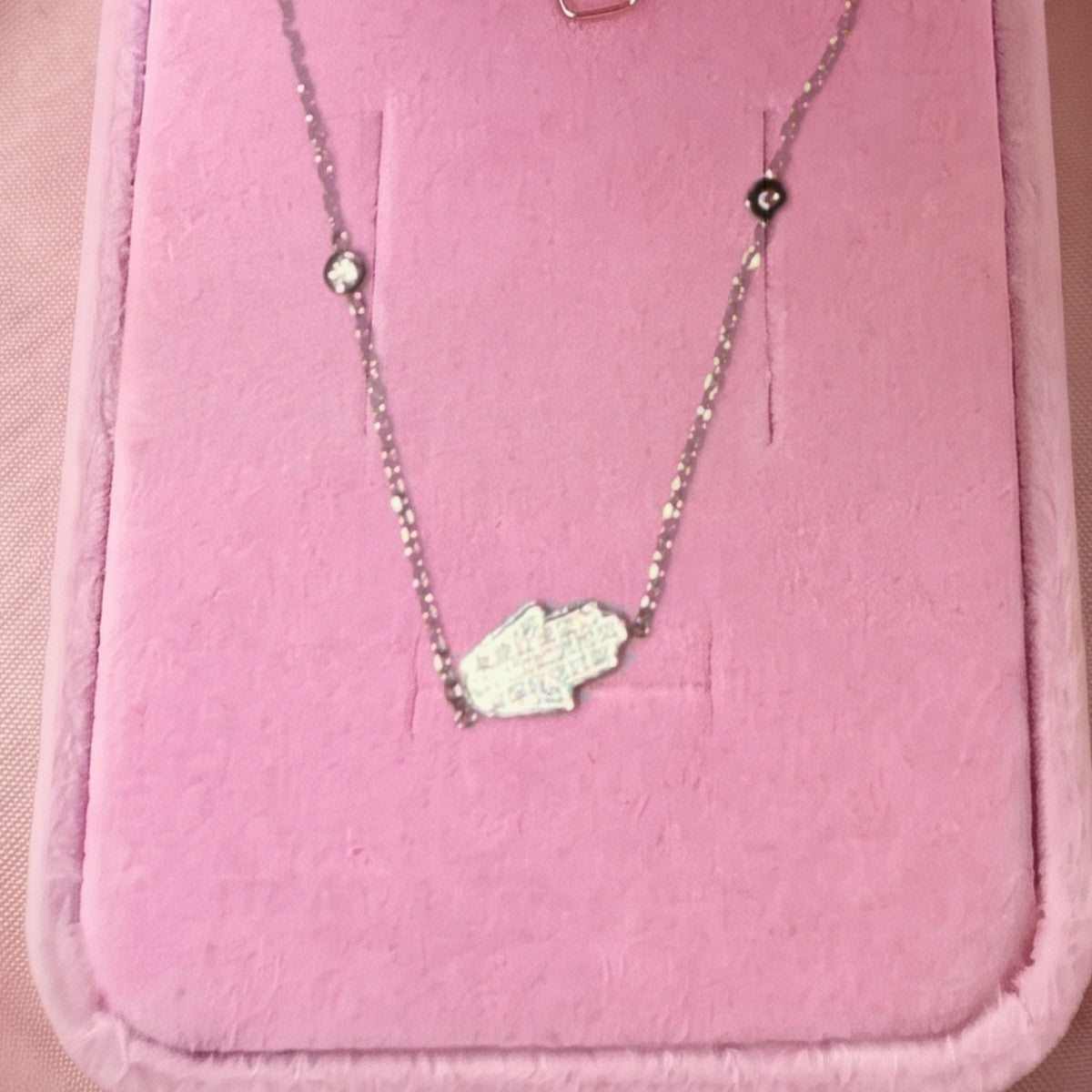 Gros plan : collier argenté à pendentif main de Fatma pavée, posé sur velours rose