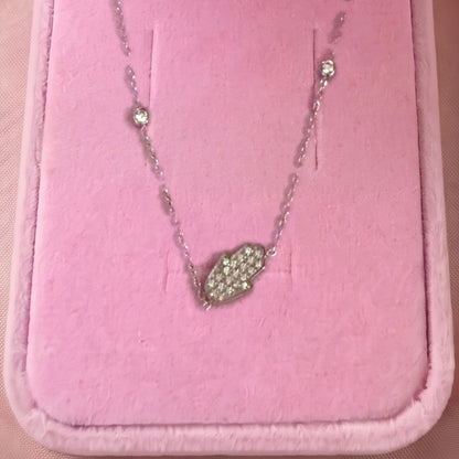 Gros plan : collier argenté à pendentif main de Fatma sertie de pierres blanches, posé sur velours rose