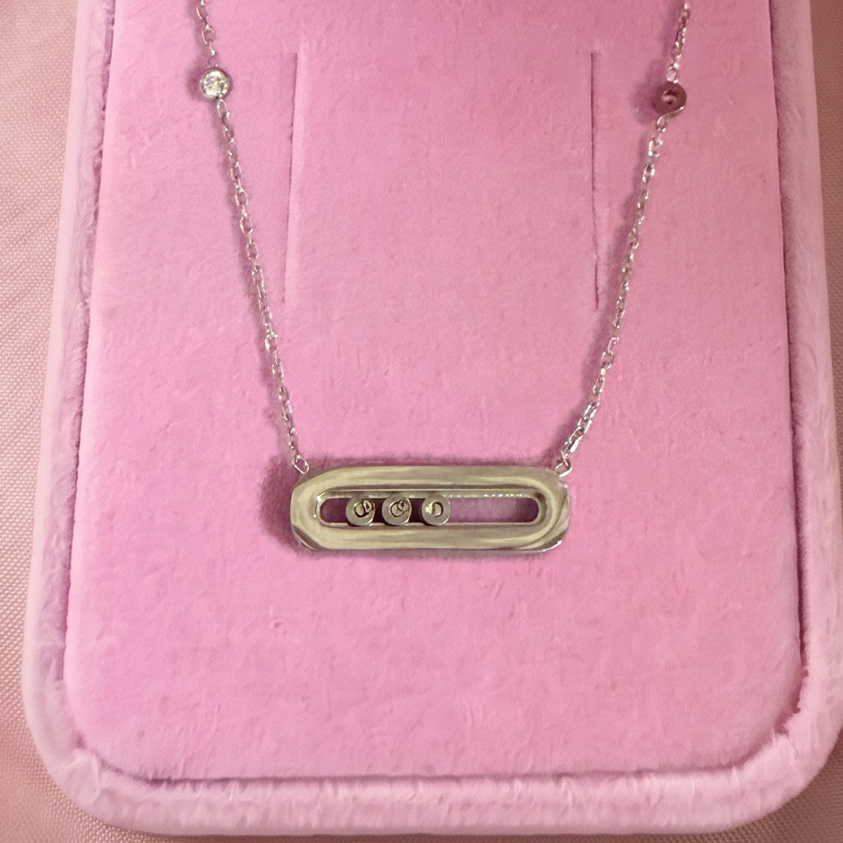 Gros plan : collier argenté à pendentif ovale et trois pierres serties, posé sur velours rose
