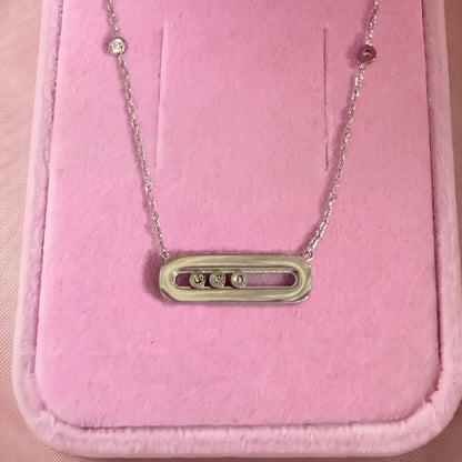 Gros plan : collier argenté à pendentif ovale et trois pierres serties, posé sur velours rose